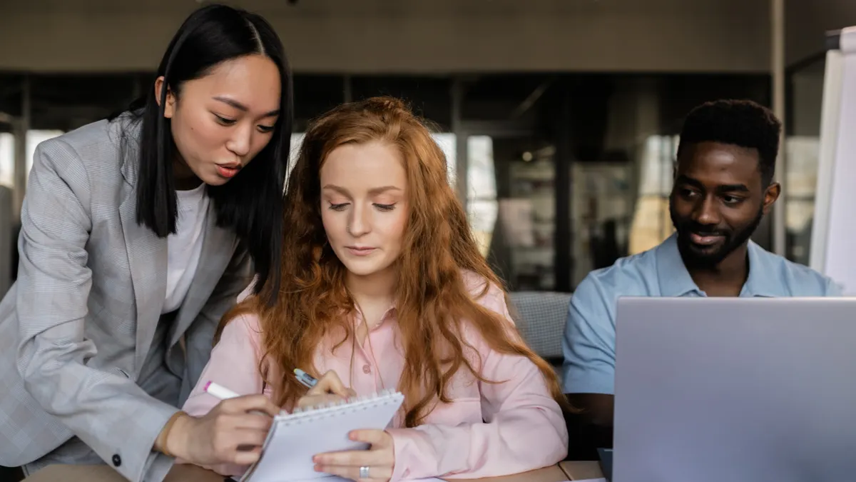 three coworkers discussing notes beside a laptop